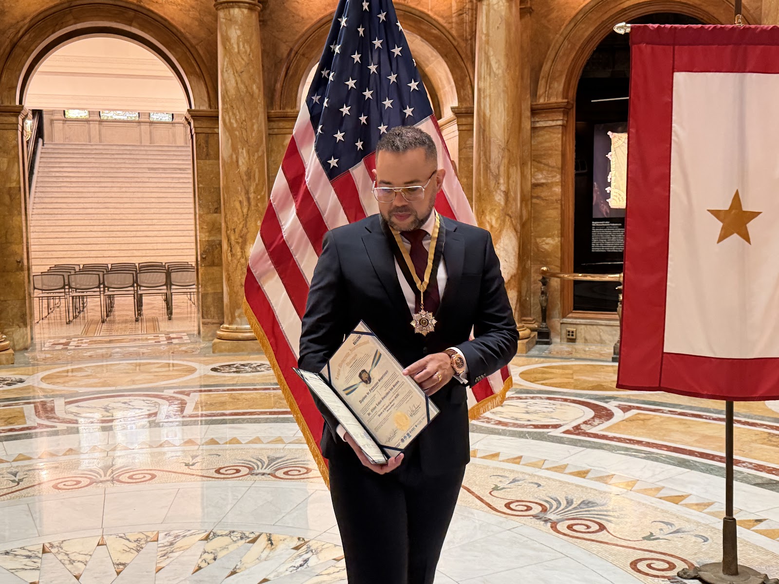 Lohan Gonçalves recebe o diploma e a medalha de Doutor Honoris Causa em Direito na State House. O título foi outorgado pela Logos University em 2025, e a entrega foi feita em 2026 pelo Prof. Dr. Marco Túlio Elias Alves.